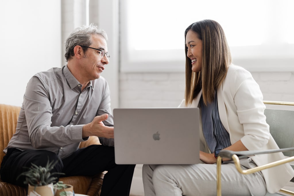 man and woman sitting together with laptop in discussion with each other