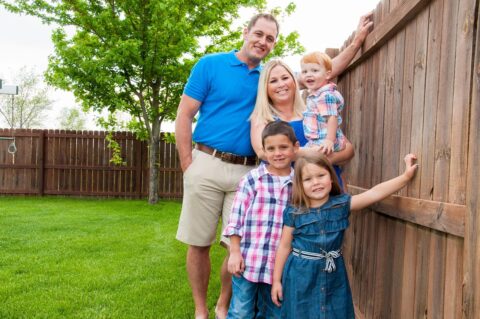 Picture of a family posing in the backyard while leaning against a brown picket fence